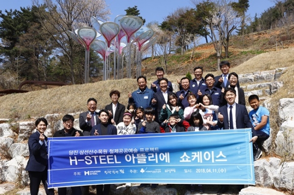 충남 당진시 고대면 삼선수목원에서 열린 ‘H-Steel 아뜰리에’쇼케이스에 참석한 관계자 및 어린이들이 ‘철, 새싹을 틔우다’라는 작품 아래에서 기념촬영을 하고 있다. / 사진 = 현대제철 제공